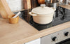 Marmite beige sur plaque de cuisson dans une cuisine avec plan de travail en bois.