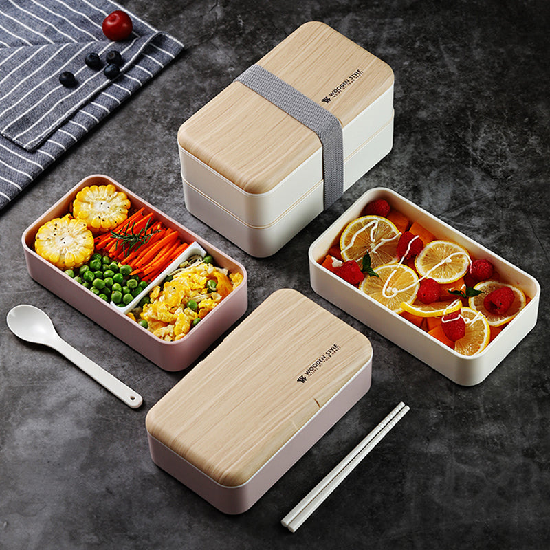 Sur cette image, on peut voir quatre lunch box ouvertes et fermées. Disposée symétriquement sur une table grise, les couvercles sont en bois et les bacs sont rose et blanc. Sur le côté gauche on voit un torchon rayé avec des myrtilles poser dessus.