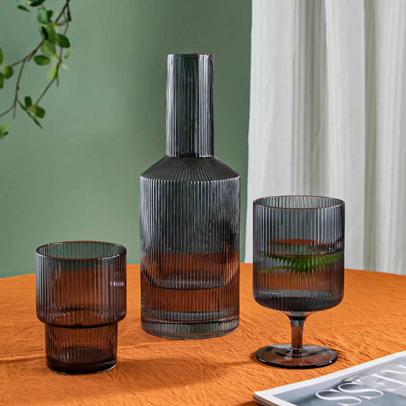 Carafe d'eau créative en verre entourée de deux verres sur une table en bois sur fond vert et blanc