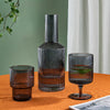 Carafe d'eau créative en verre entourée de deux verres sur une table en bois sur fond vert et blanc