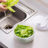 Essoreuse à salade manuelle blanche classique en plastique sur un plan de travail avec une personne qui lave de la salade dans l'évier