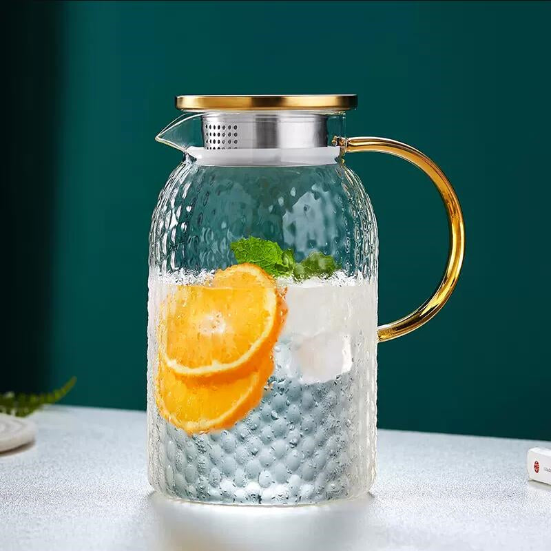 Carafe d'eau en verre avec couvercle en acier inoxydable contenant des zestes d'orange sur une table grise sur fond vert