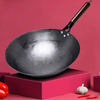 Poêle wok traditionnelle en fer forgé à la main sur fond rouge avec une gousse d'ail et des piments en bas à droite et un poivron rouge en bas à gauche