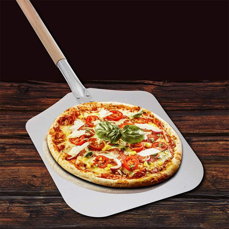 Pelle à pizza longue en métal avec un manche double en bois contenant une pizza sur une table en bois sur fond noir 